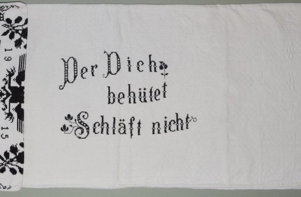 Langseite eines Polsterbezugs, sogenannte Polsterziechen, aus Marpod von 1915, bestickt mit der Inschrift „Der Dich behütet schläft nicht“