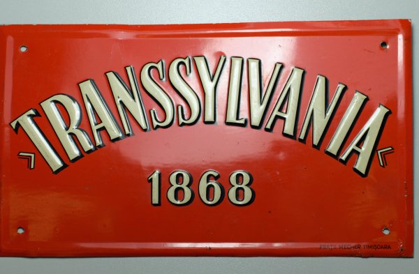 Plakette der Transsylvania Versicherung. Rechteckige Blechtafel mit rotem Untergrund und weißem Schriftzug 